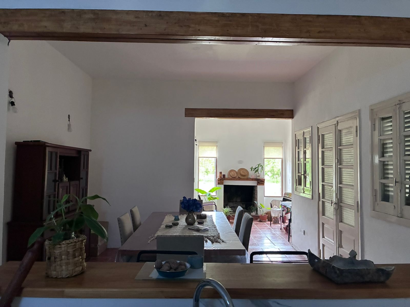 Sala de jantar rústica com vigas de madeira e lareira — projeto Chacra JE, por Atelier de Diseño Interior - Luján Macia, em Río Colorado